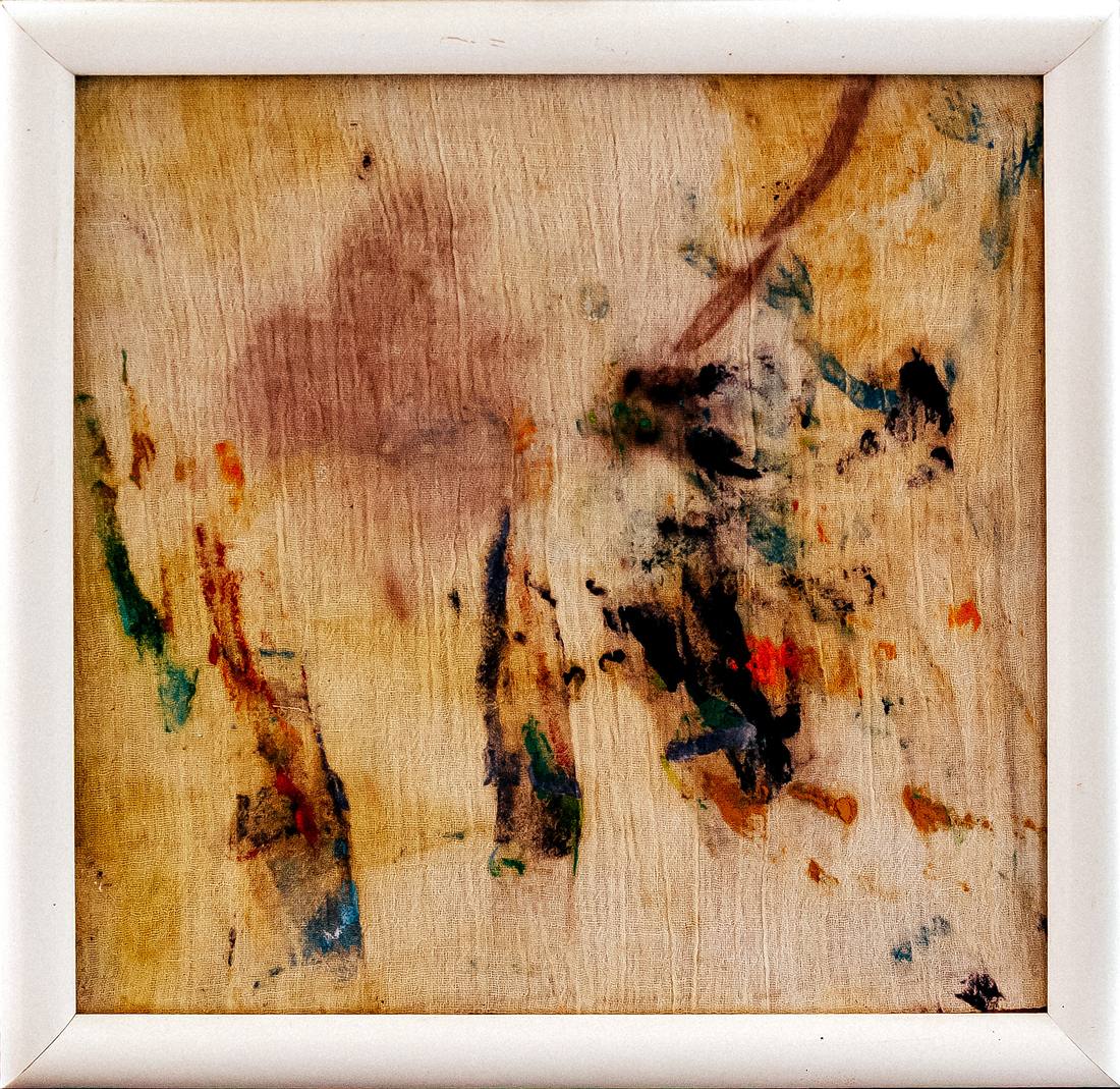 Creased pale fabric in a white frame, a mauve stain at the top, black, green, blue and orange marks lower down.